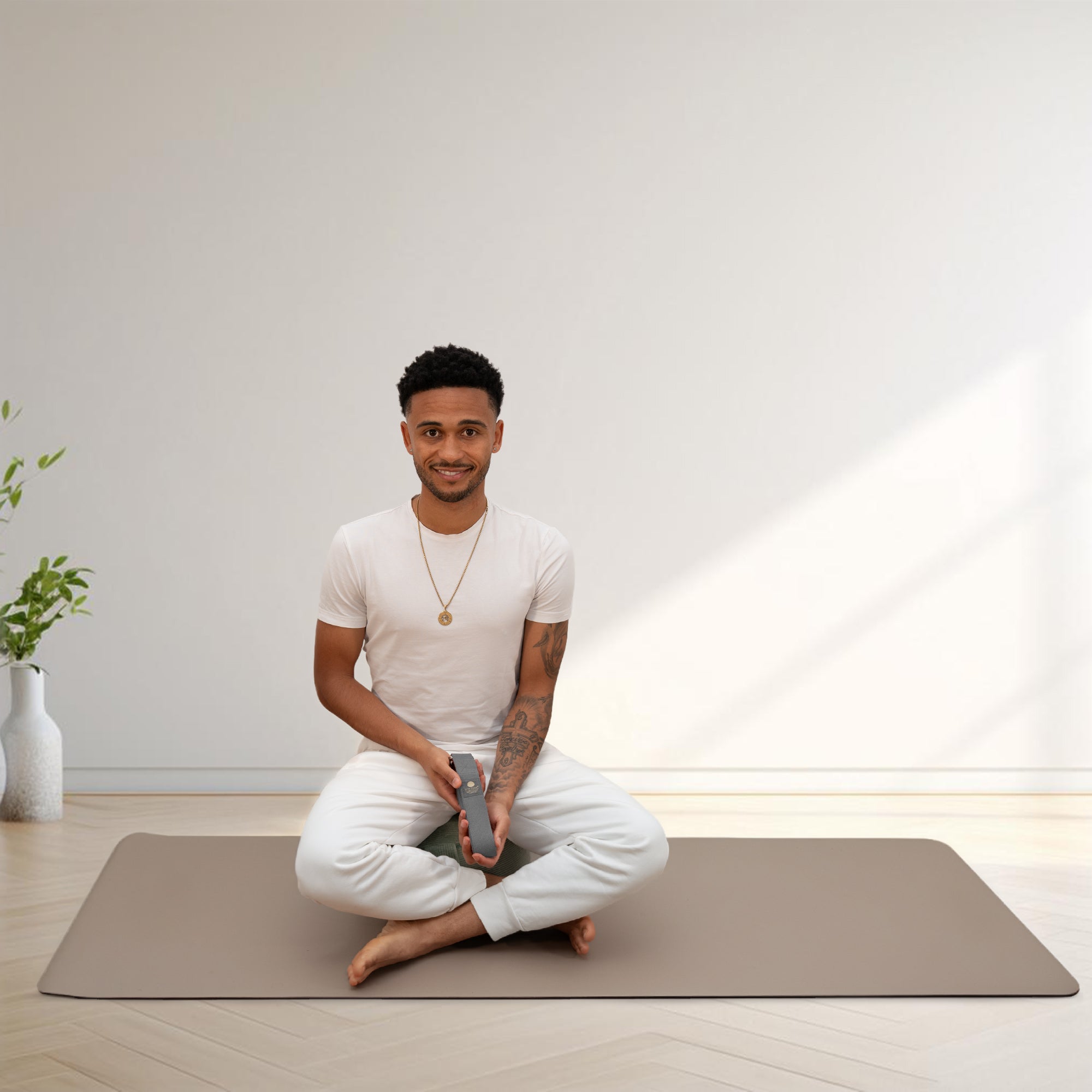 Mann sitzt im Schneidersitz und hält aufgerollten Yogagurt aus Baumwolle – ökologisch und fair produzierter Yoga Belt